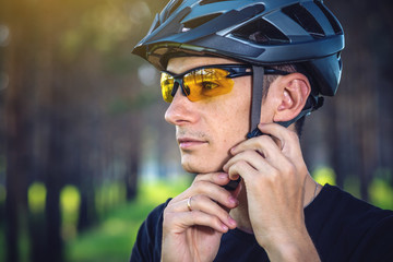 Cyclist is wearing a sports helmet on his head in the background of green nature. Protection during...