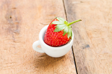 Strawberry cherry red in a small white cup and placed on a wooden background
