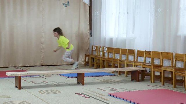 Girl athlete makes somersaults on tatami and jump through the bench