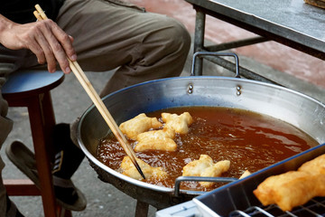 Man fring dough for sell in morning market of Thailand with  blurred deep fried dough in tray.