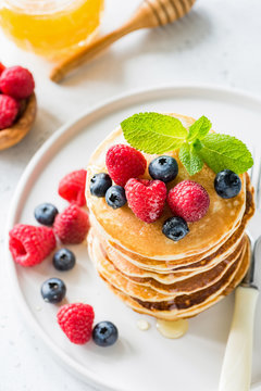 Pancakes with fresh berries and honey on white plate. Top view, selective focus