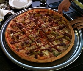 Pizza big, huge size on the table in the pizzeria. Pizza with mushrooms, salami, chicken, pineapple, cheese, pepper, tomatoes and greens,