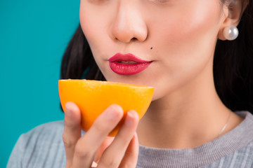 Healthy food. Close-up of dmiling lovely pinup asian girl holding orange over blue background.