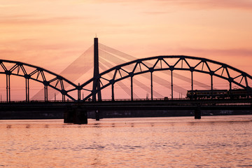 Fototapeta na wymiar railroad metal bridge silhouette over river of Daugava in Riga, Latvia in dark red sunet