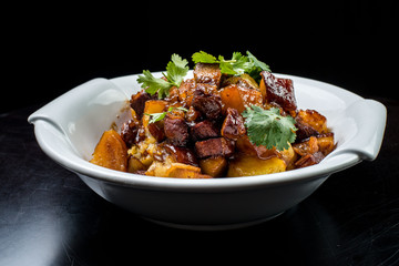Chinese beef stew with young potatoes in sweet sauce, in white plate on black background