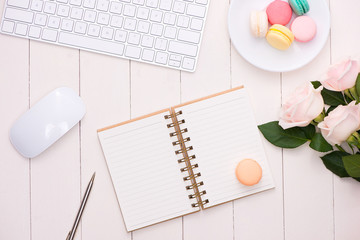 White desk with colorful macaroons, keyboard and open notebook.