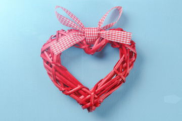 Red woven straw heart on blue background. Symbol of love or health