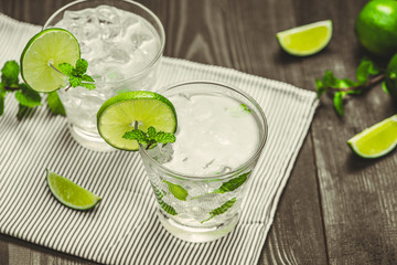 Fresh lime cocktail with ice cubes on wooden background