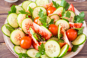 Vegetable salad of fresh cucumbers, tomatoes, parsley and sesame seeds on a plate
