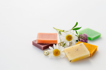Small pieces of natural handmade soap and fresh meadow flowers of chamomile and clover on a light background. 