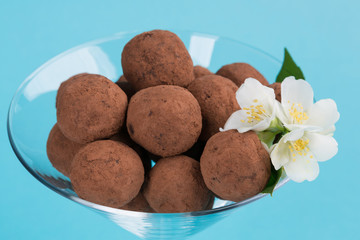 round chocolate candies in a glass, decorated with white flowers, on a turquoise background, macro photo