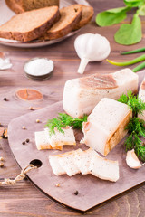 Sliced salted lard with garlic and dill on a cutting board on a wooden table