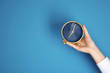 Female hand holding alarm clock on color background. Time management concept