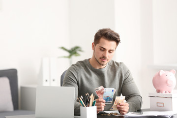 Young man counting money at table indoors