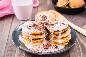 A pile of pancakes stuffed with fruit yoghurt and sprinkled with grated chocolate on a plate on a wooden table
