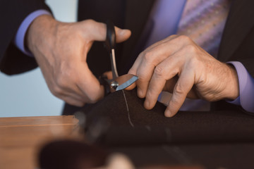 Obraz na płótnie Canvas Mature tailor cutting fabric in atelier, closeup