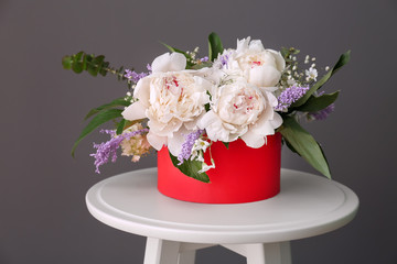 Box with beautiful peony flowers on stool against grey background