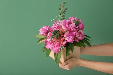 Woman holding box with beautiful peony flowers on color background