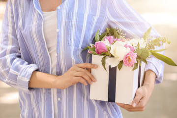Woman holding gift box with beautiful peony flowers outdoors, closeup