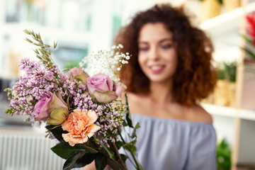 Floristic masterpiece. Selective focus of a flower bouquet being in hands of a cheerful attractive woman