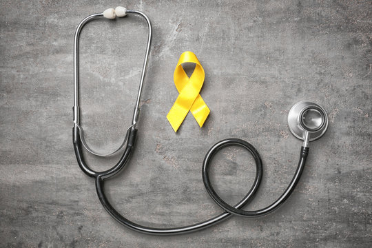 Yellow ribbon and stethoscope on grey background. Cancer concept