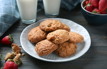 Plate with delicious oatmeal cookies and fresh strawberries on dark wooden background