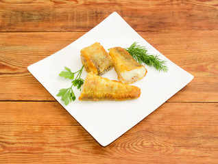 Slices of the fried fish and greens on square dish