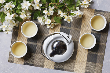 White porcelain Asian tea set with green tea and jasmine on  bamboo napkin, top view.