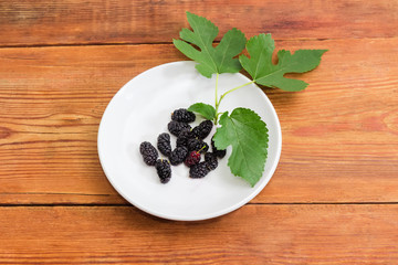 Black mulberry fruits on the saucer on rustic table