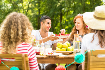 Handsome man offering fruit to his girlfriend while having a garden party with friends