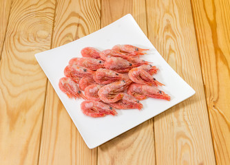 Frozen shrimps on square dish on a wooden surface