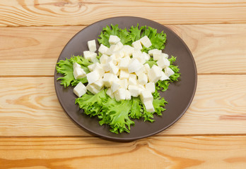Diced mozzarella cheese on lettuce leaves on brown dish