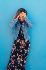 lachende frau mit einem langen sommerkleid steht vor einer blauen wand