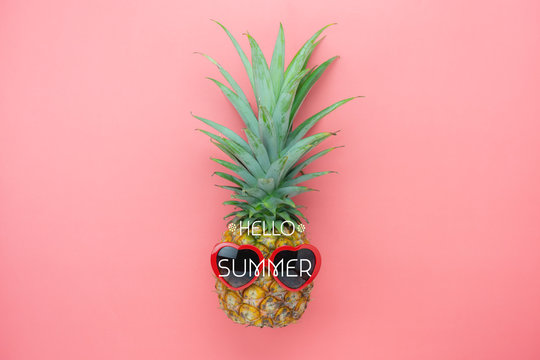 Table top view aerial image of summer & travel beach holiday in the season background concept.Flat lay sign objects on season.Pineapple wear red sunglasses on pink paper with word hello seasonal.