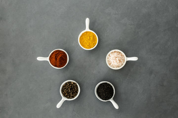 Top view of bowls with spices arranged in a circle on a grey background