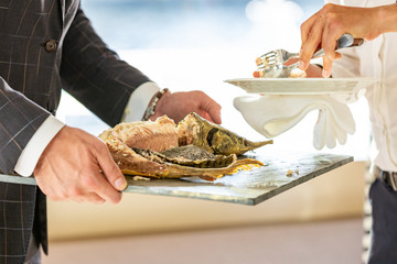 Obraz na płótnie Canvas the waiter hands cutting baked sturgeon in the restaurant