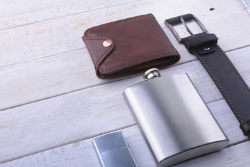 Gadgets and accessories for men on light wooden background. Fashionable men s belt, wallet, lighter, Stainless hip flask and pen.