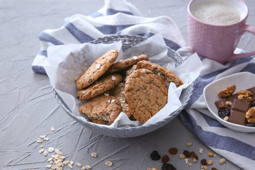 Wicker bowl with delicious oatmeal cookies and cup of coffee on table