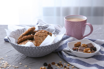 Wicker bowl with delicious oatmeal cookies and cup of coffee on table