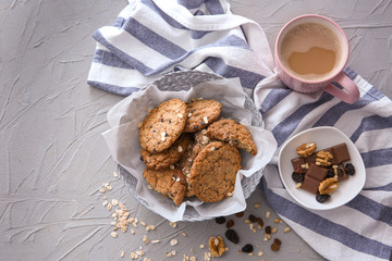 Wicker bowl with delicious oatmeal cookies and cup of coffee on table