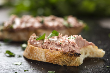 Bitten Liverwurst Sandwich with chopped parsley on a dark slate