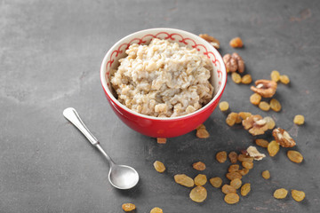 Bowl with tasty oatmeal, raisins and walnuts on grey background
