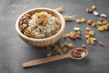 Fototapeta premium Bowl with tasty oatmeal, raisins and nuts on grey background