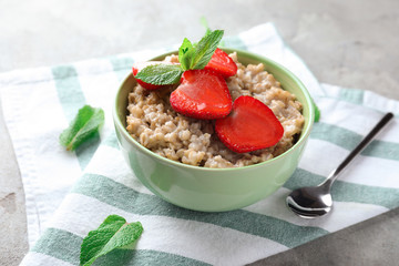 Bowl with tasty oatmeal and strawberry on grey background