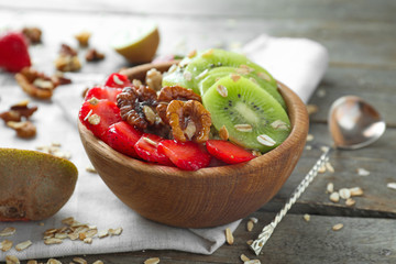 Bowl with tasty oatmeal, fresh strawberry and sliced kiwi on wooden table
