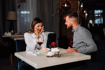 Portrait of happy and surprised young woman receiving present from boyfriend while sitting in cafe
