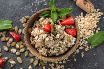 Bowl with tasty oatmeal, strawberry and pumpkin seeds on grey textured background