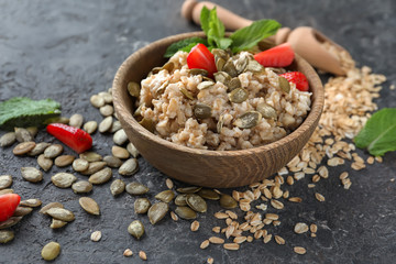 Bowl with tasty oatmeal, strawberry and pumpkin seeds on grey textured background