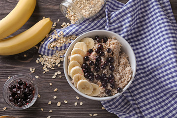 Bowl with tasty oatmeal, berries and banana on wooden table
