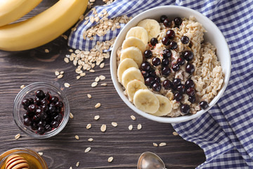 Bowl with tasty oatmeal, berries and banana on wooden table